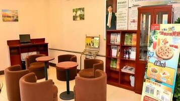 A hotel lobby with seating arrangements, a reception desk, informational posters, and a menu board.