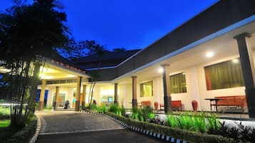 A building with a covered entrance, outdoor seating, and a pathway leading to the entrance.