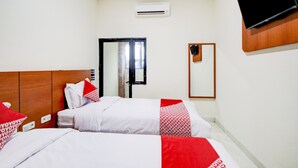 Ein Hotelzimmer mit zwei Betten, einem an der Wand montierten Fernseher, einer Klimaanlage und einem Spiegel.