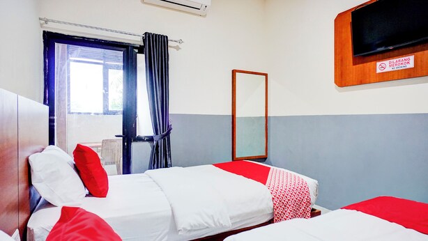 Ein Hotelzimmer mit zwei Betten, einem Fernseher, einem Spiegel und einem Fenster mit Vorhängen.