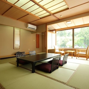 Una habitación tradicional japonesa con suelo de tatami, una mesa baja con cojines y puertas correderas.