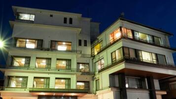 A multi-story hotel with a modern design, featuring balconies on the upper floors and a parking area in front.