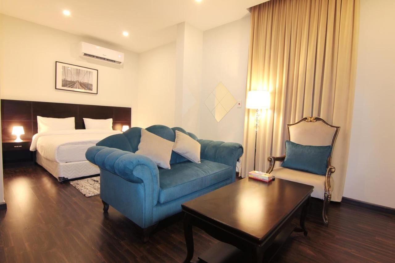 Una habitación de hotel con una cama, un sofá azul, una mesa de centro de madera y una lámpara.