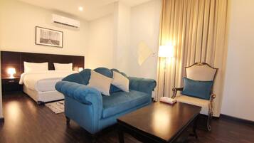 Una habitación de hotel con una cama, un sofá azul, una mesa de centro de madera y una lámpara.