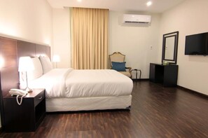 Ein Hotelzimmer mit einem großen Bett, einem Nachttisch mit Lampe, einem Sessel, einem Fernseher und einer Klimaanlage.