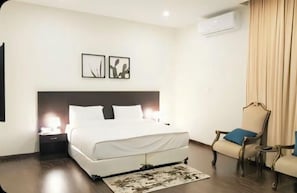 Hotellihuone, jossa on sänky, yöpöytä, tuoli ja taideteos seinällä.