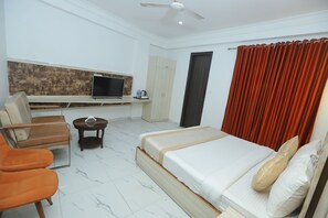 A hotel room with a bed, a desk with a television, a chair, a small table, and a wardrobe.