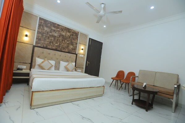 A hotel room with a bed, a desk, two chairs, a sofa, a ceiling fan, and a door.
