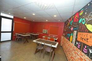 A classroom with tables and chairs, a projector screen, and a wall with colorful drawings and text.