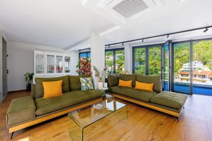 Un salon moderne avec deux canapés verts, une table basse en verre et de grandes fenêtres donnant sur un paysage verdoyant.
