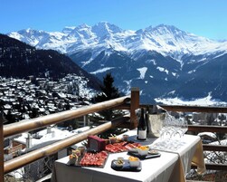 Mesa posta com comida e bebidas, com vista para uma cordilheira coberta de neve.