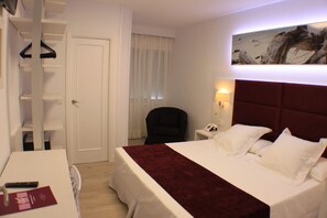 Una habitación de hotel con cama, escritorio, silla, armario y un cuadro en la pared.