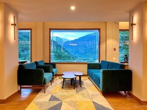 Quarto com uma janela grande, dois sofás, uma mesa pequena e um tapete estampado.