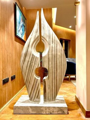 A modern interior with a unique abstract sculpture on a marble base, wooden paneling on the walls, and a framed artwork above. - Bookmark Resort (Manali)