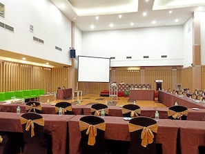 A conference room with rows of tables, chairs, and a stage area.