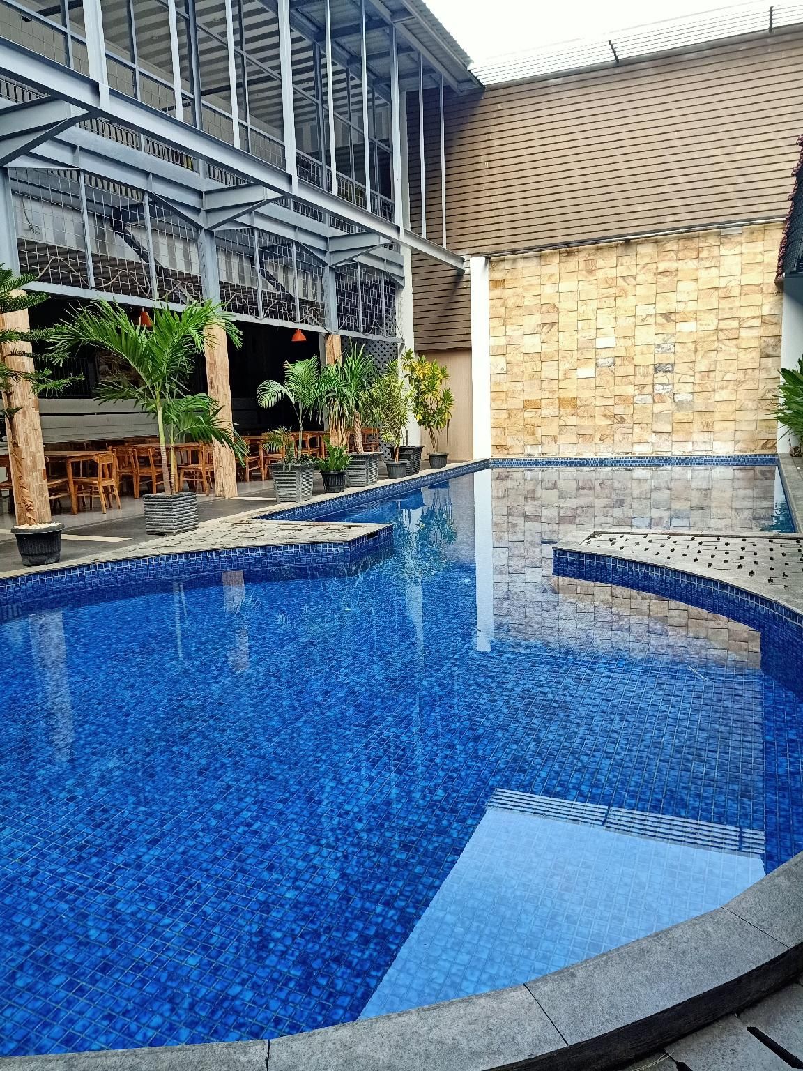 A swimming pool with a tiled edge, surrounded by a building with a tiled roof and a stone wall.