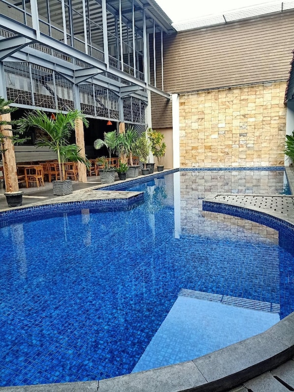 A swimming pool with a tiled edge, surrounded by a building with a tiled roof and a stone wall. - Grand Nanggroe (Banda Aceh)