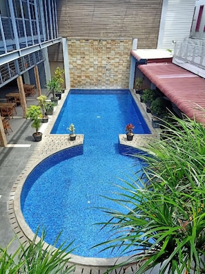 A rectangular swimming pool with a tiled edge, surrounded by potted plants, and a stone wall in the background.
