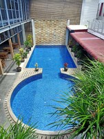 A rectangular swimming pool with a tiled edge, surrounded by potted plants, and a stone wall in the background.