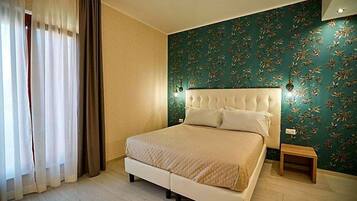A bedroom with a bed, curtains, a nightstand, and a wall with a floral pattern.