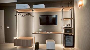 A modern hotel room with a bed, a desk, a television, and a minibar.