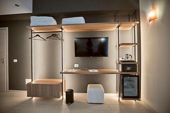 A modern hotel room with a bed, a desk, a television, and a minibar. - Castrichella Boutique Hotel (Fiumicino)