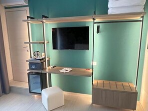 Habitación compacta con cama, escritorio pequeño, televisor y refrigerador minibar.