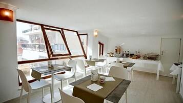 A dining area with tables and chairs, a buffet setup, and large windows offering a view of the city.