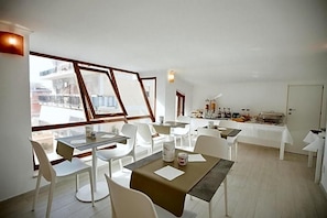 Una zona de dinar amb taules i cadires, un aparador tipus buffet i grans finestres amb vistes a la ciutat.