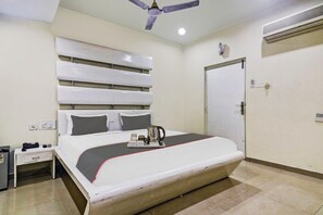 A hotel room with a large bed, a desk, a chair, a ceiling fan, a door, and an air conditioning unit. - The Crown Hotel (Hyderabad)