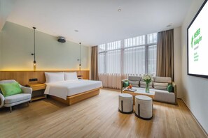 A hotel room with a bed, a sofa, a chair, a coffee table, and a screen displaying hotel information. - Holiday Inn Wuyi Mountain Water Village (Nanping)