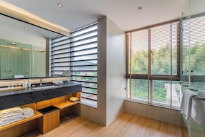 Un baño moderno con un espejo grande, encimera negra, almacenaje de madera y una ventana con persianas.