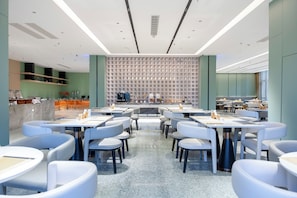 Un restaurante moderno con mesas y sillas blancas, una barra central y un muro con diseño.