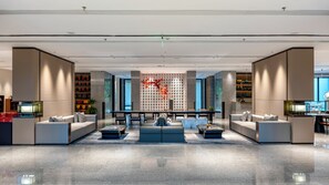 Un vestíbulo moderno con una zona de estar central, una pared decorativa con un estampado floral rojo y una zona de bar con estantes llenos de botellas.