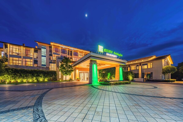 Entrada de hotel con fachada iluminada, cielo despejado y luna visible.