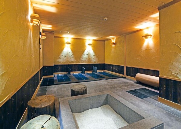 Una sala de sauna con bancos, un banco de madera y una pileta de piedra.