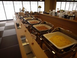 Montaje tipo bufé con diversos alimentos en recipientes metálicos, una vitrina de cristal y una barra con artículos adicionales.