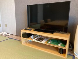 Un televisor sobre un soporte de madera, un control remoto, un libro y un altavoz pequeño.