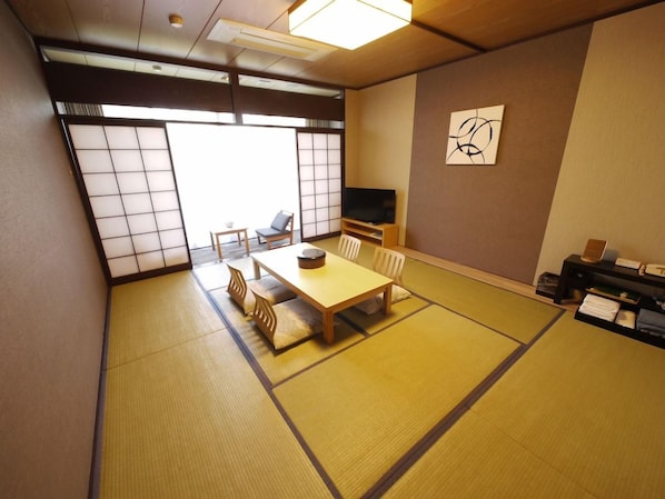A tatami mat room with a low table and chairs, a television, and a sliding door. - Route-inn Grantia Wakamiya (Miyawaka)