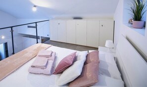 A modern bedroom with a bed, towels, pillows, a potted plant, and a view of a balcony. - Design Central Apartment (Bergamo)