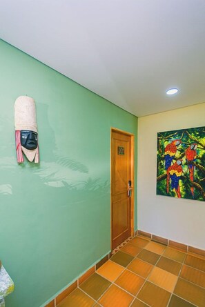 A hallway with a green wall, a wooden door labeled '101', and a colorful painting of parrots. - Hotel Bambu Guatape (Guatapé)