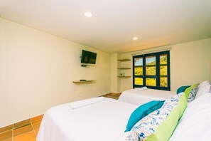 A hotel room with two beds, a television mounted on the wall, and a window with a view of greenery. - Hotel Bambu Guatape (Guatapé)