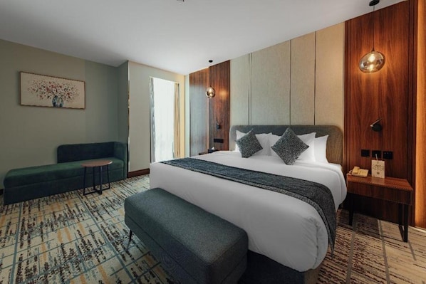 Habitación de hotel moderna con una cama grande, zona de estar y vistas al exterior.