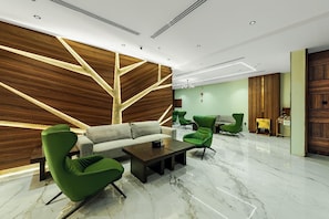 Un vestíbulo moderno con un sofá, sillas verdes, una mesa de centro de mármol y una pared de acento de madera.