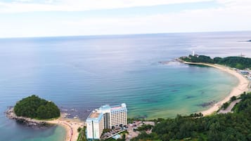 An aerial view of a coastal hotel with a beach, a small island, and a lighthouse in the distance.
