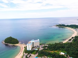 An aerial view of a coastal hotel with a beach, a small island, and a lighthouse in the distance.