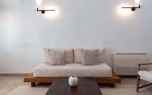 Sala de estar minimalista com sofá, mesa de centro de madeira e duas luminárias fixadas na parede.