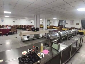 Una cafetería amplia con varias mesas y sillas, una barra de buffet con recipientes de comida y una estación de bebidas de autoservicio.