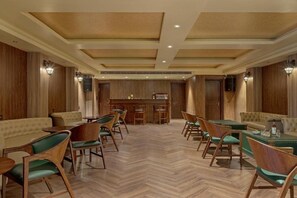 Comedor de hotel con paneles de madera, sillas tapizadas en verde y un suelo con estampado de espiga.