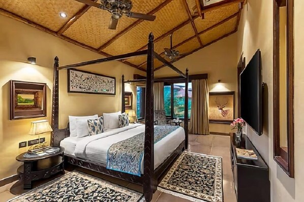 A four-poster bed with a canopy, a television on the wall, and a framed picture above the bed.